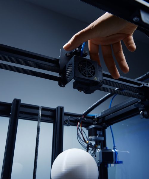 A gender-neutral hand modifying settings in 3d printer, to finish printing round white object from recycled plastic. Futuristic concept of new working possibilities for small businesses by 3D printing